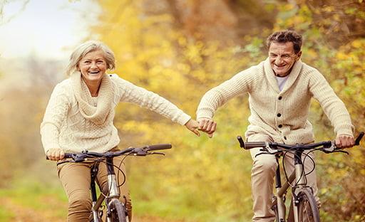 Elderly couple riding bikes while holding hands in the fall